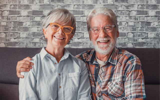 A couple sitting side-by-side, both wearing eyeglasses