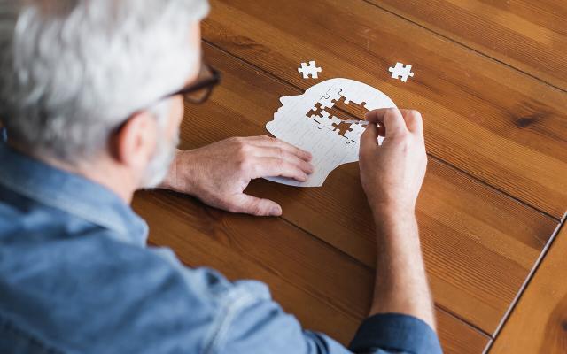 An older adult assembling a puzzle shaped like a person's head